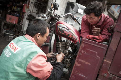 Foshan, Guangdong, China aa March 16 2013: Curbside Streetview, Unidentified mechanic repairs motorcycle in Shunde District of Foshan City, Guangdong Province in Southern China.