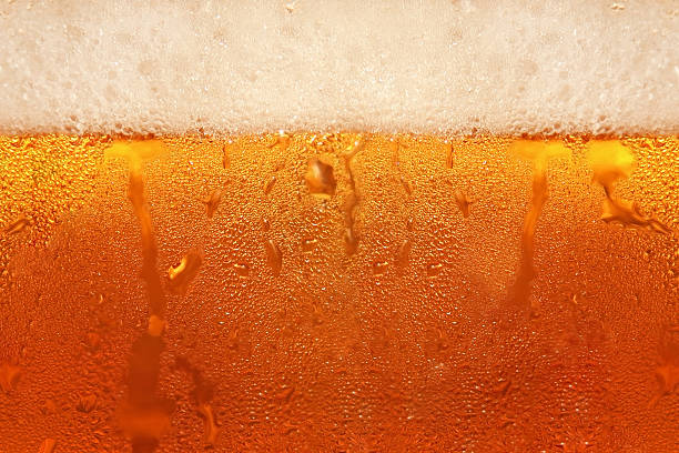 The top layer of foam forming on a newly-poured beer Beer foam in glass taken closeup as background. beer stock pictures, royalty-free photos & images