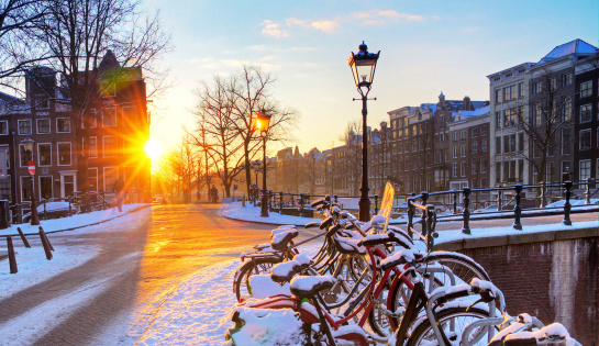 Sunrise over the canal streets of Amsterdam, the Netherlands, with bicycles covered in snow on a beautiful winter day. HDR