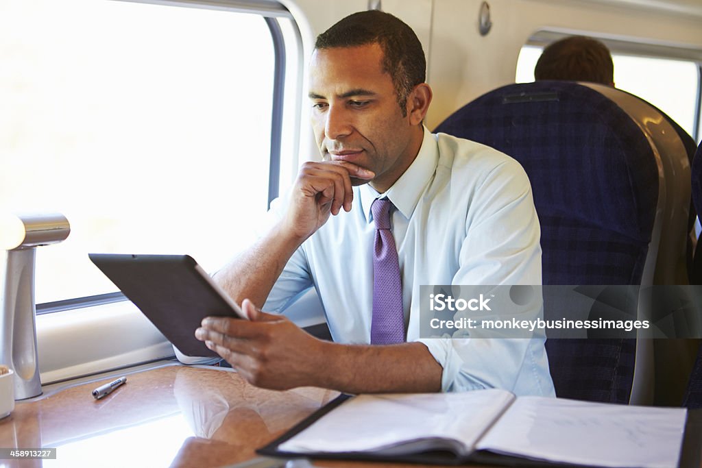 A businessman using a tablet on a train Businessman Commuting On Train Using Digital Tablet resting chin on hand Train - Vehicle Stock Photo