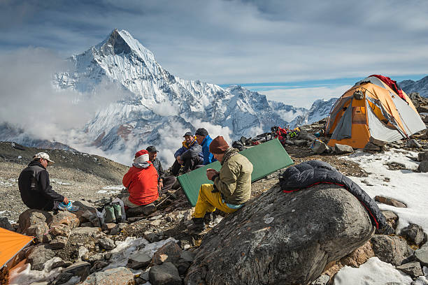 Sherpa mountaineers at expedition base camp Himalaya Nepal "Deurali, Nepal - 2nd November 2012: Team of Sherpa mountaineers sitting on rocks amongst base camp tents overlooked by the iconic pyramid peak of Machapuchare (6993m) deep in the Himalayan mountain wilderness of the Annapurna Conservation Area." base camp stock pictures, royalty-free photos & images