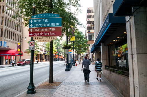 Atlanta, GA, USA - August 3, 2011: Two black men walk down the sidewalk beside Peachtree Street in the heart of downtown Atlanta. Bank of America, Hooters, and the Westin Peachtree Plaza are among the businesses around this block. A sign points the way to Turner Field, Underground Atlanta, and Olympic Park