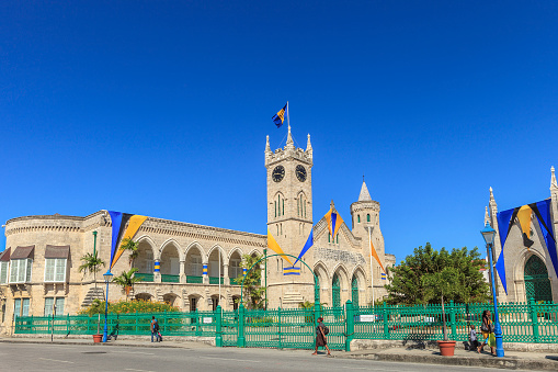Bridgetown, Barbados - November 20, 2011: People strolling in front of the Parliament Building in a Sunday morning. The building is a masterpiece of Gothic Architecture, built in 1874 of local coral limestone and strategically placed in downtown Bridgetown.