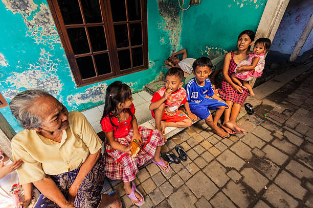Group of Kids in a Small Village, Java, Indonesia "Cianjur, Indonesia - June 23, 2012: Group of small kids with an adult and a elder woman sitting along one alley of a rural village in central Java" central java province stock pictures, royalty-free photos & images