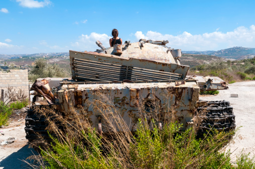 Qana, Lebanon - September 2, 2010: A young Lebanese woman sits atop an abandoned tank in southern Lebanon, looking at a landscape that has known much war.