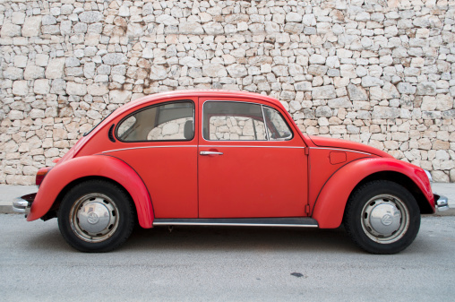 Valencia, Spain – September 01, 2012: Red Volkswagen Beetle parked in front of a stone wall on a street in Valencia.