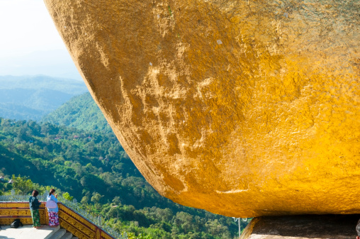 Kyaiktiyo, Myanmar - October 30, 2011: Two Burmese women stand beneath the Golden Rock, or Kyaiktiyo Pagoda, in Myanmar's Mon State. Famous for how it is precariously perched on the ledge, it is said that the rock is balanced on a hair of the Buddha.