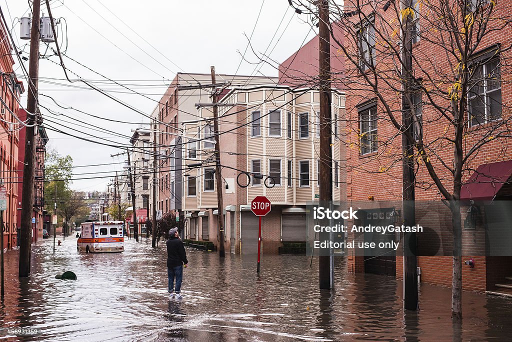 Hurricane Sandy: man standing on a flooded street "Hoboken, New Jersey, USA - October 31, 2012: Man standing on the flooded street is talking to someone left in the building, ambulance car in the background" Flood Stock Photo