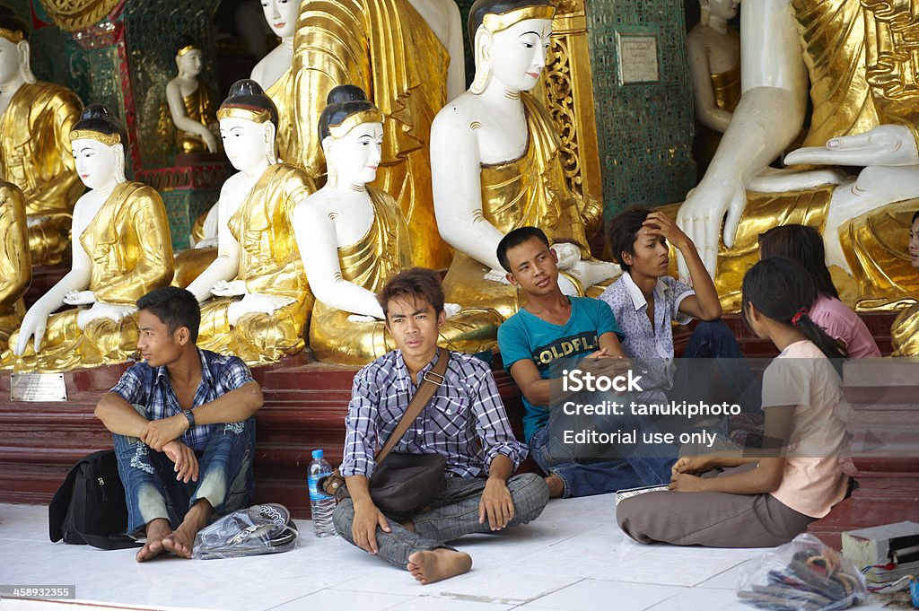 Pilgrims in Shwedagon Pagoda complex "Yangon, Myanmar - May 1, 2012: young burmese pilgrims have some rest seated in the shadow of a pavillion of the Shwedagon Pagoda complex." Adult Stock Photo