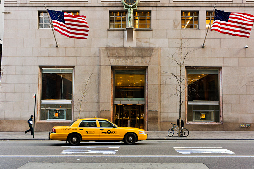 New York, United States - January 20, 2012: Taxi and people in front of the famous Tiffany jewelry store in the Fifth Avenue in Manhattan New York. Tiffany + CO luxury jewelry store in the Fifth avenue in Manhattan New York. This american company founded in 1837. Tiffany's flagship store,in the photo, was inaugurated in 1940 at the corner of the Fifth Avenue with and 57th street and was the location of the famous Breakfast at Tiffany's movie with Audrey Hepburn. The firm runs now more than one hundred stores around the world.