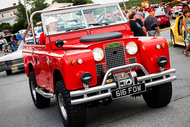 Dartmouth, Nova Scotia, Canada - August 23, 2012: Land Rover Series II truck driving through a crowded parking lot.  Lot filled with classic cars for the annual Cruisin' the Dub event held by A and W restaurant.  Multiple vehicles entering lot, with others parked and many people visible in background admiring the vehicles.  Land Rover has a man driving.