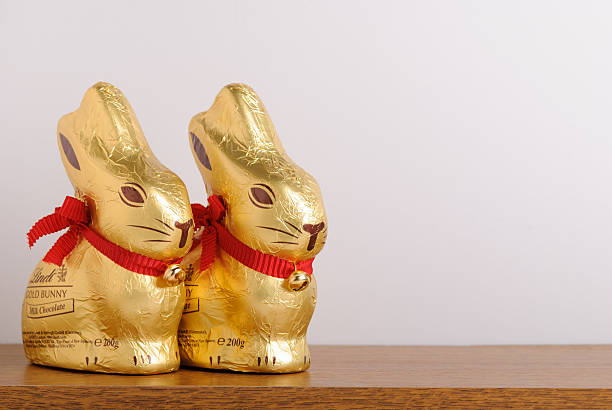 Two Lindt Easter Gold Bunnies on Shelf "Rustington, UK - April 10, 2012: Two Lindt Easter Gold Bunnies on a shelf. These bunnies are made from milk chocolate. The Lindt company has manufactured chocolate since 1845. Every year the Lindt gold bunnies are popular at Easter." chocolate bunny stock pictures, royalty-free photos & images