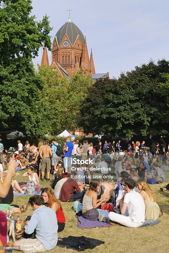 Carnival of Cultures in Berlin "Berlin, Germany - May 26, 2012: The Carnival of Cultures is a multicultural festival. This festival is held on Whit weekend since 1996. In the background there is the Holy Cross Church. The focus of BlAcherplatz with many guests, young people of different Nations. The young people sitting in the grass and make party." Adult Stock Photo