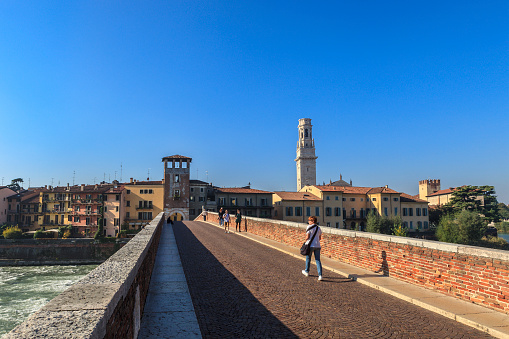 Verona, Italy - October 23, 2012: People strolling on the ancient Ponte Pietra, a five-arched bridge that crosses the river Adige. It is a precious testimonial of the Roman period.