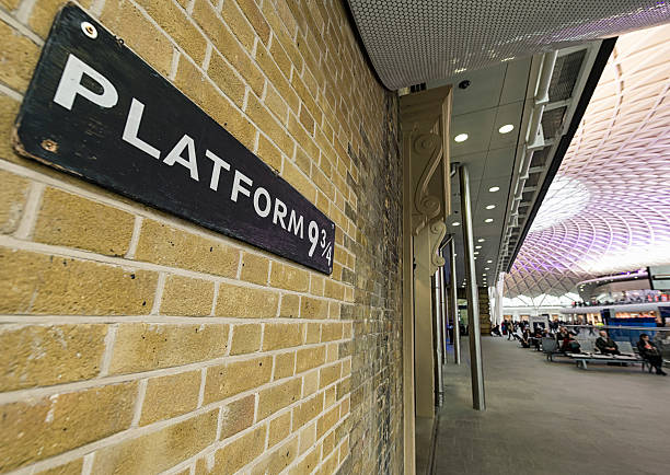 Platform Nine and Three Quarters at King's Cross Station London, UK - May 2, 2012: Close-up of a sign for the ficticious Platform 9 and 3/4, with people in the background within the departure concourse of King's Cross Station. In J.K. Rowling's Harry Potter book series, the Hogwarts Express train can be boarded from this hidden platform. editorial architecture famous place local landmark stock pictures, royalty-free photos & images
