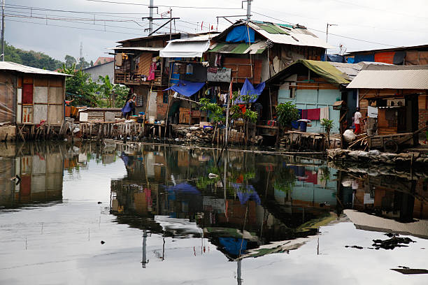 Slum Area "Jakarta, Indonesia - November 19, 2009: Slum Area in Jakarta, Indonesia. Many people in Jakarta lives in slum areas. It`s not aloud to build houses everywhere. There are two women depited in front of the houses." jakarta slums stock pictures, royalty-free photos & images