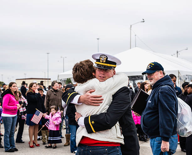 Sailor Returns From Deployment "Norfolk, Virginia, USA - November 4, 2012: A horizontal shot of a sailor who has just returned from deployment with the US Navy on the USS James E. Williams. A woman hugs the sailor, while in the background crowds of other family members await their loved ones who have yet to disembark from the returned ship." military deployment photos stock pictures, royalty-free photos & images