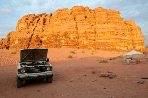 Wadi Rum, Jordan - November 15, 2010: A Toyota Land Cruiser sits parked outside a desert encampment in Wadi Rum, its hood open, as the light from a rising sun hits an escarpment