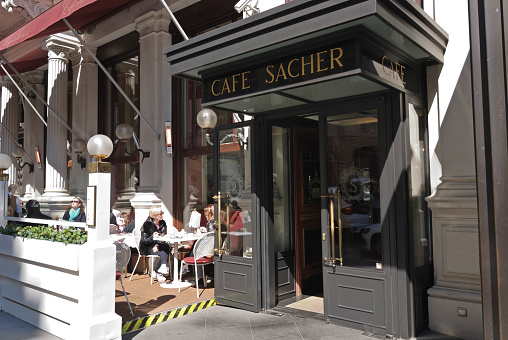 Vienna, Austria - April 9, 2012: People drink coffee in garden next to entrance of Cafe Sacher. This is part of famous Sacher Hotel in Vienna. It is situated in Vienna city center behind the Opera house.