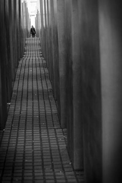 Man Walking in the Holocaust Memorial, Berlin, Germany "Berlin, Germany- November 16, 2011: Man walking among the cement blocks of the monument to the Murdered Jews of Europe in central Berlin.  The memorial consists of a 19,000 square meters site covered with 2,711 concrete slabs or stelae." berlino stock pictures, royalty-free photos & images