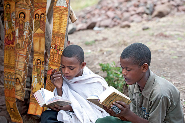Novices in an orthodox monastery is reading a holy book "Lalibela, Ethiopia - November 8, 2011: A novice of an orthodox monastery is sitting in the compound of the rock hewn churches of Lalibela in Northern Ethiopia and is reading a book written in the old language of the church, called Geez." ethiopian orthodox church stock pictures, royalty-free photos & images