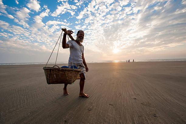 Man carrying seafood walking on the beach, Bangladesh "Cox's Bazar, Bangladesh - February 10, 2013: A man is carrying seafood in barrel on shoulder walking on the beach of Cox's Bazar, Bangladesh." bay of bengal stock pictures, royalty-free photos & images