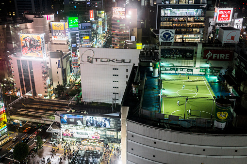 Tokyo, Japan - October 6, 2012: View of Shibuya district at night Tokyo Japan. People playing soccer in a rooftop stadium while the crowd is walking on the streets.