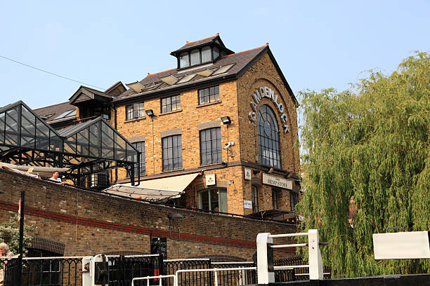 London, United Kingdom - May 29, 2012: In spring sunshine, a  well-known retail outlet (the Hemp Store) is viewed from the Regents Canal in Camden Lock, in North-West London, England. Some bystanders, possibly shoppers or tourists can also be seen. The Camden Lock area hosts an open-air market, many pubs, restaurants and stores and is a magnet for tourists, shoppers and locals. A canal-side willow tree and some lock mechanisms can also be seen. The Hemp Store is a clothing outlet in Unit 9, East Yard, Camden Lock, London, specialising in eco-friendly casual clothing.