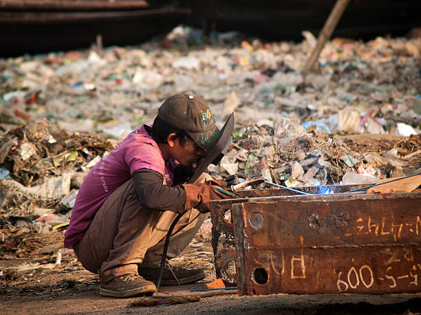 Child labour remains social norm in Bangladesh "Dhaka, Bangladesh - January 23, 2012: Young male work as a Shipyard welder surrounded by rubbish heap at Ship breaking yard in Dhaka city, capital of Bangladesh." child labor stock pictures, royalty-free photos & images