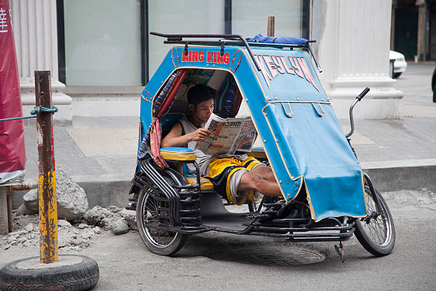 Cab Driver Reads Newspaper "Manila, Republic of the Philippines - April 21, 2012: On Ongpin street a tricycle cab driver reads newspaper while waiting for fares as another cab driver talks to him in Manila's Binondo (Chinatown) district. Binondo is considered to be the oldest Chinatown in the world and was established in 1594." philippines tricycle stock pictures, royalty-free photos & images