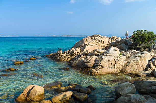 Sardinia "Cala di Volpe, Italy - September 10, 2012: Tourists on the bay cliffs taking a sun bath, in the foreground the transparent waters of the sea." Cala Di Volpe stock pictures, royalty-free photos & images