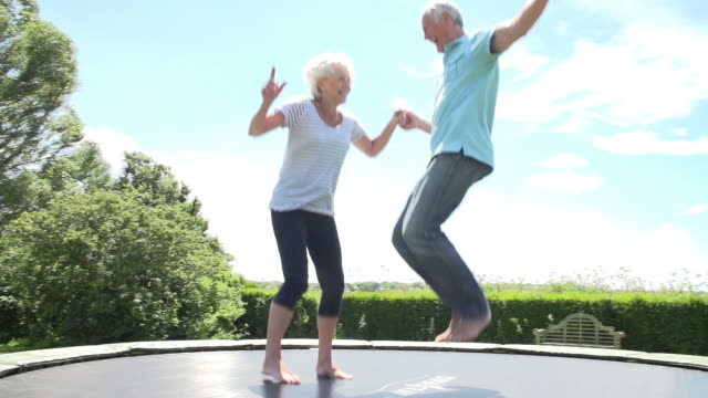 Senior Couple Bouncing On Trampoline In Slow Motion