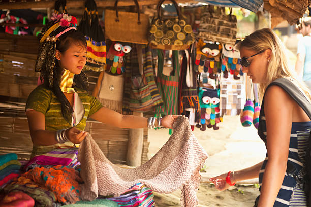 Fabrics of the Long Neck Karen Tribe "Chiang Mai, Thailand - November 21, 2012: A tourist browses as a hill tribe woman presents authentic fabrics woven by the women of the indigenous Long Neck Karen tribe in a rural village near Chiang Mai in northern Thailand." padaung tribe stock pictures, royalty-free photos & images