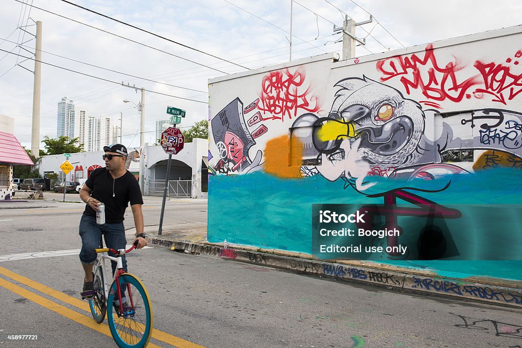 Miami Biking Wynwood Street Graffit Art Mural Travel Destination "Miami, United States - December 2, 2012: A man on a colorful bike rides down the graffiti lined streets of Wynwood with a beer in hand." City Life Stock Photo