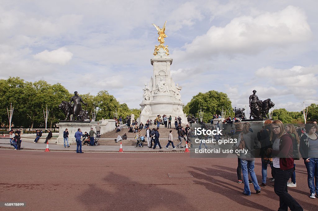 Victoria Memorial "London, United Kingdom - October 2, 2012: Victoria Memorial. Tourists rest and take pictures at the steps of Victoria Memorial, which is situated just opposite the Buckingham Palace, in the centre of Queen's Gardens. This memorial consists of several sculptures and belongs to the listed buildings of the United Kingdom, which are very well protected by authorities. Recently, the Memorial served as a centrepiece of the stage for Queen Elizabeth II's Diamond Jubilee Concert. Along with the Buckingham Palace it is a very popular tourists' destination, with many of them taking photographs in front of it." British Culture Stock Photo