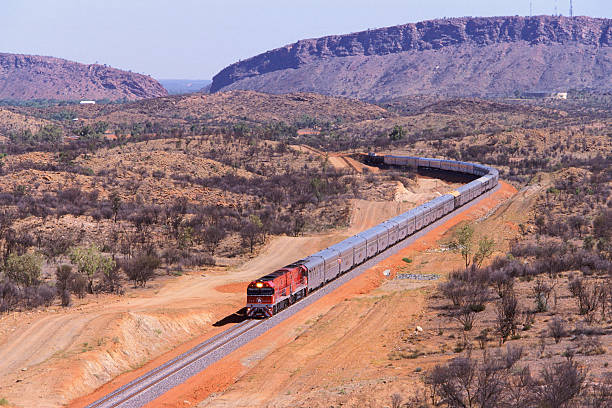 The First Ghan train to Darwin departs Alice Springs "Alice Springs, Australia - February 2, 2004: The first Ghan passenger train to Darwin departs Alice Springs with the spectacular MacDonnell Ranges in the background.  The extra long VIP train is mid-way through its inaugural 2969km transcontinental journey from Adelaide in the South to Darwin in the North.  The first train departed Adelaide February 1 and arrived in Darwin to a huge welcome on February 3, 2004.  The journey from the Mediterranean South through Australias Red Centre to the tropical Top End takes the Ghan 54hrs.  The Ghans symbol is a camel and its handler, in recognition of the pioneering Afghan cameleers who opened up the outback of Australia in the mid-19th century." 2004 2004 stock pictures, royalty-free photos & images