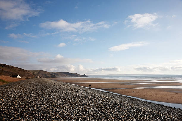 Newgale, Wales - February 25, 2012: Couple walking along the pebble breakwater at Newgale beach in Pembrokeshire and another couple walking along the sandy beach