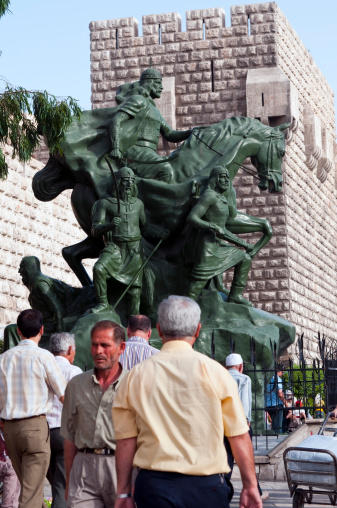 Damascus, Syria - June 6, 2010: Pedestrians walk past a statue of Saladin, also spelled Salahdin, outside the city walls of the Old City. Salahdin is perhaps best known for his victories against the Crusaders.