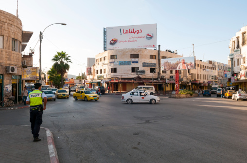 Jenin, West Bank, Palestinian Territories - October 23, 2010: A Palestinian policeman stands at a main intersection in the northern West Bank city of Jenin. Traffic, shops, and billboards are at the intersection.