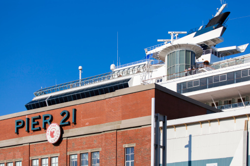 Halifax, Nova Scotia, Canada - September 12, 2012: Pier 21 in downtown Halifax with a cruise ship visible behind building and in background.  Three people stand on boat and peer off the side into Halifax.  Pier 21 is Canada's National Museum of Immigration in Halifax and attracts conferences and events and houses a cafe, a gift shop and other vendors.  It is the last remaining ocean immigration shed in Canada.