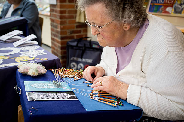 Bobbin Lacemaking Demonstration "Wantage, England - June 9, 2012: A senior woman from Wantage Lacemakers group demonstrates Bobbin lacemaking at the cafeteria outside Vale and Downland Museum during Wantage summer festival. This self-help group is committed to ensuring this ancient craft continues to the young generation." lacemaking photos stock pictures, royalty-free photos & images