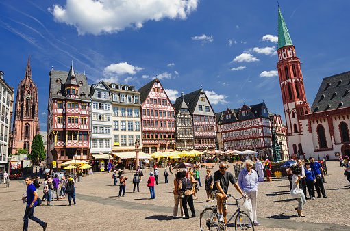 Frankfurt, Germany - May 29, 2012: Tourist and local people at the Römerberg on a beautiful summer day in Frankfurt, Germany. The Römerberg is the historical square in the old town of Frankfurt and the city´s major tourist attraction. The original half-timbered houses at the east row have been destroyed during the 2nd World War bombing in 1944 and were rebuilt in the 1980th. The east side of the square consist of the Cathedral (Kaiserdom Sankt Bartholomäus) on the left, the reconstructed half-timbered houses, the Fountain of Justice and the church of St. Nicolas on the right.