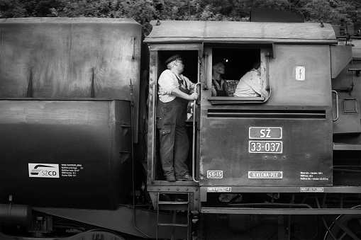Bled, Slovenia - June 30, 2012: On a summer evening, a train crew is busy shunting an old fashioned steam train in the station in Bled, Slovenia. The train is a tourist attraction using old rolling stock on the historic Bohinj Railway track, opened in 1906. Two of the three-man crew are watching the driver. One of the engineers is wearing a miners-type lamp to help see in the gloom of the cabin.