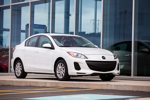 Dartmouth, Nova Scotia, Canada - December 2, 2012: A new Mazda 3 sedan vehicle in front of a Mazda dealership.  Vehicle is on prominent display in front of dealership and inside front window a sitting area can be seen.  Known as the Alexa in Japan is was introduced as a 2004 model.  Model pictured is the current and second generation of the Mazda 3 (as of December 2012).