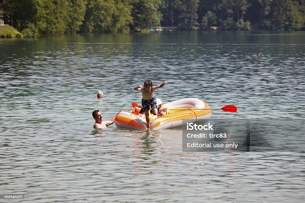 Boy jumping into the lake "Bled, Slovenia - July 2, 2012: Boy jumping into the lake from a rubber dinghy. A man is holding the boat steady and another child is in the dinghy and a woman swimming alongside" Activity Stock Photo