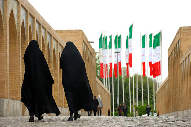 Women in Nitjab and Iran flags "Isfahan, Iran - April 6, 2013: Women covered by traditional black Nitjab walking towards Iranian flags on bridge in Isfahan, Iran" iranian culture stock pictures, royalty-free photos & images