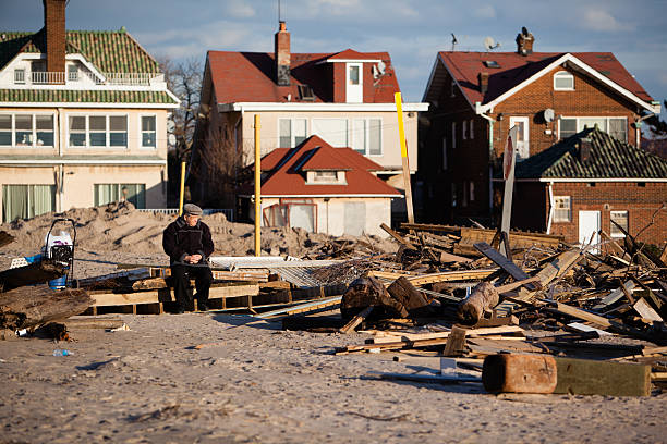 Old man sitting next to ruined homes after Sandy hurrican New York City, USA - December 11, 2012: Old man sitting between ruins at Brighton Beach. After about 2 months, parts of a damaged homes still on the Brighton Beach as a consequences of the Sandy hurricane. hurrican stock pictures, royalty-free photos & images