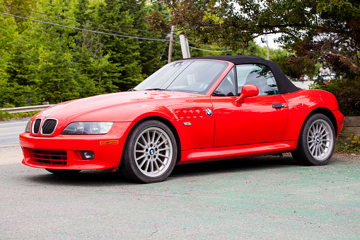 Bedford, Nova Scotia, Canada - June 3, 2012: A red BMW Z3 is parked in a driveway with the black convertible top in the upright and closed position.  In the background the passing street along with a wooded area are pictured.  The BMW Z3 was introduced in 1996 after first appearing in the 1995 James Bond film GoldenEye.  The appeal of the Z3 lead to variants of the vehicle being offered over its lifespan including a coupe version introduced in 1999 and an M performance version of both the convertible and coupe.