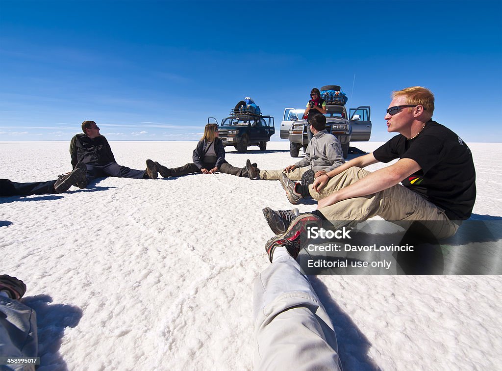 Rest at Uyuni "Uyuni, Bolivia - June 25, 2008: People, tourist sitting in circle with legs together having rest and photo session on Uyuni Salt Flats in Bolivia.  In background are cars with photographer and blue sky above them." Blue Stock Photo