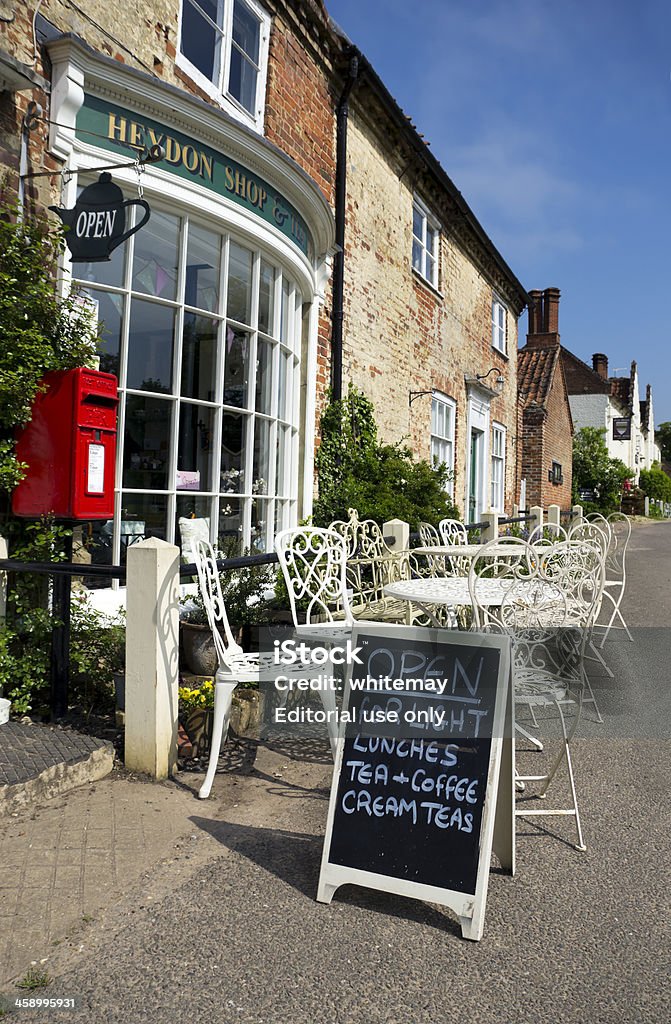 Village cafe "Heydon, England - May 22, 2012: The village shop and tea rooms with old cottages in the quaint, old fashioned Norfolk village of Heydon. The village has no road passing through it so has remained peaceful and timeless: it is frequently used in films and TV productions because of these qualities. Mentioned in the Domesday Book as High-Down, it became Norfolks first conservation area in 1971. The church is famous for its wall paintings and the pub, the Earle Arms, is named after one of the ancestral families from Heydon." Cafe Stock Photo